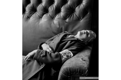 Eine junge Frau in einem Mantel, die Rot Kreuzbinde am Arm. liegt tot in einer Sofaecke, Schwarzweißfoto