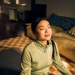 Eine Person sitzt mit geschlossenen Augen auf dem Boden und genießt die Sonnenstrahlen