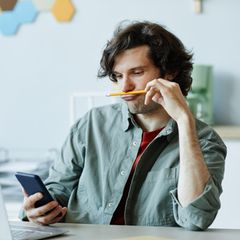 Mann schaut auf sein Smartphone und spielt mit einem Bleistift