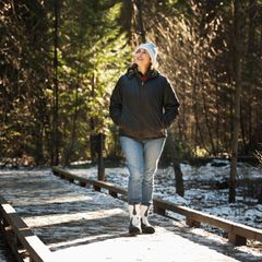 Eine Frau mit weisser Mütze wandert im Winter auch den Wald