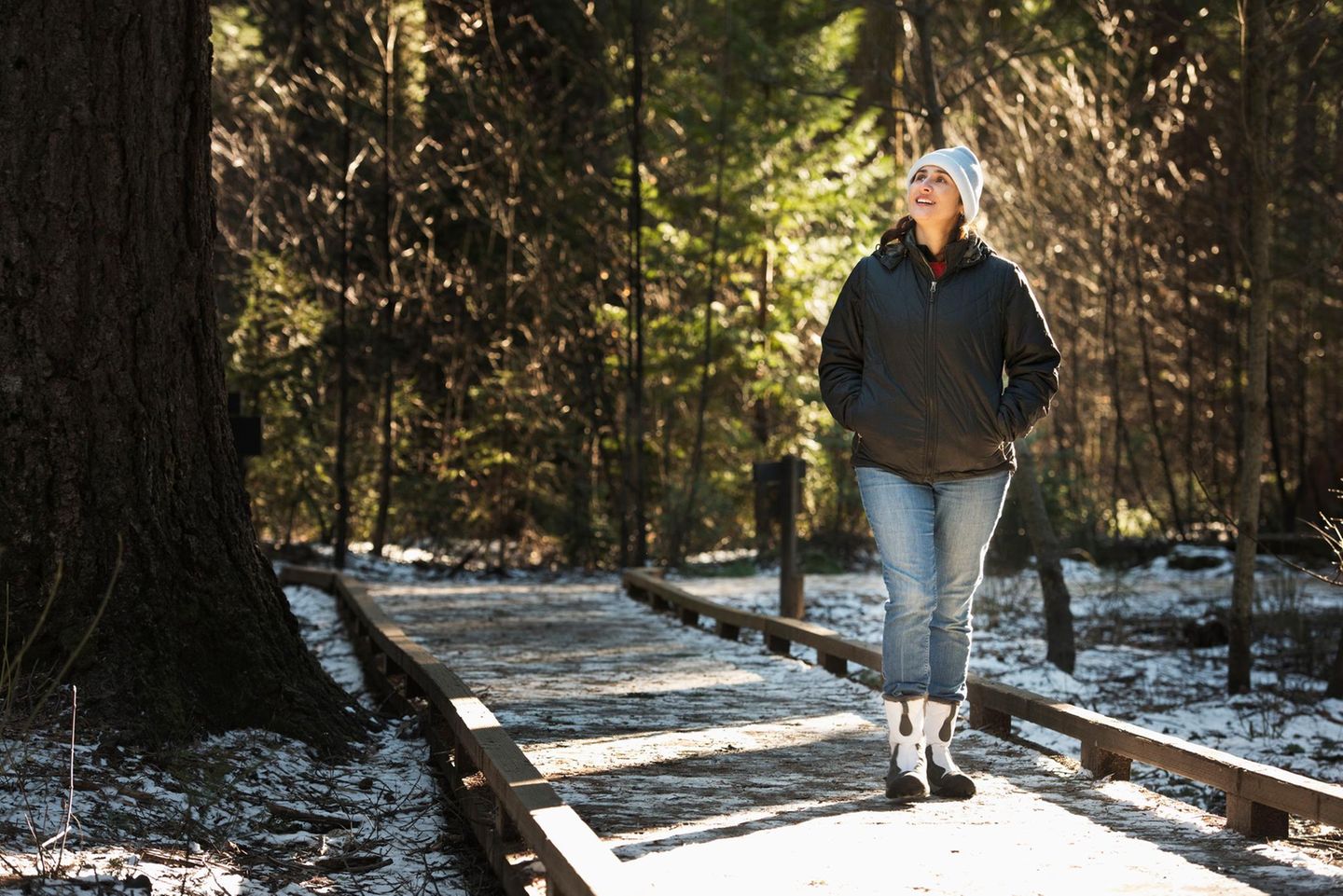 Eine Frau mit weisser Mütze wandert im Winter auch den Wald