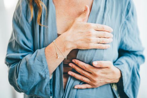 Frau tastet ihre Brust ab und trägt eine Bluse