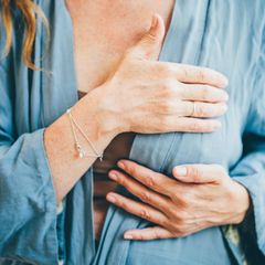 Frau tastet ihre Brust ab und trägt eine Bluse