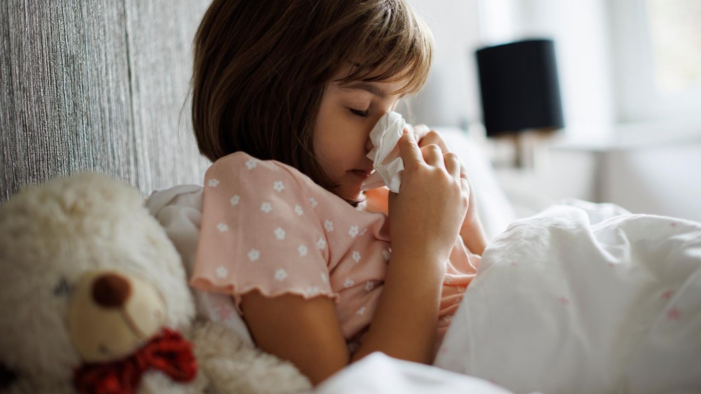 Kleines Mädchen mit Grippe putzt sich die Nase im Bett