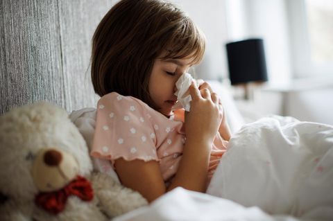 Kleines Mädchen mit Grippe putzt sich die Nase im Bett