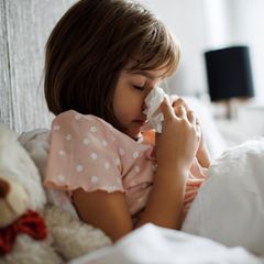 Kleines Mädchen mit Grippe putzt sich die Nase im Bett