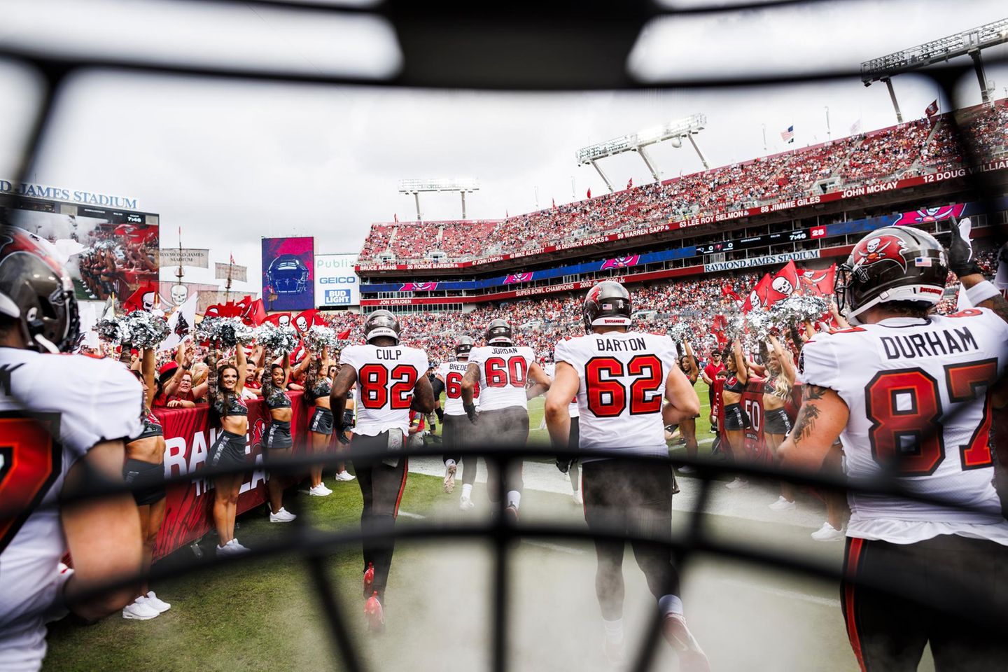 Auftakt eines American-Football-Matches: Die Tampa Bay Buccaneers laufen an den Cheerleadern vorbei auf das Feld, zur obligatorischen Vorstellung der Teams vor dem Beginn des Spiels. Das ungewöhnliche Foto dazu schoss Kyle Zedaker, indem er seine Kamera hinter dem Helmgitter befestigte – und so den Betrachtenden einen beinahe intimen, authentischen Einblick verschaffte, weil er die Perspektive der Profis einnahm.   