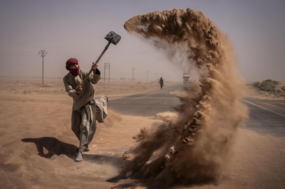 Person schippt am Straßenrand Sand weg