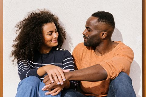 Ein Paar hockt vor einer Wand, lächelt sich an und hält einander die Hand