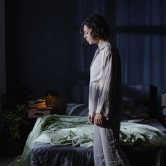 Frau mit Schlafstörungen steht im Schlafanzug müde vor ihrem Bett