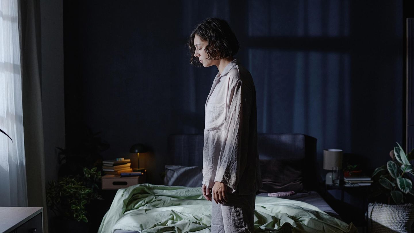 Frau mit Schlafstörungen steht im Schlafanzug müde vor ihrem Bett