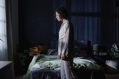 Frau mit Schlafstörungen steht im Schlafanzug müde vor ihrem Bett