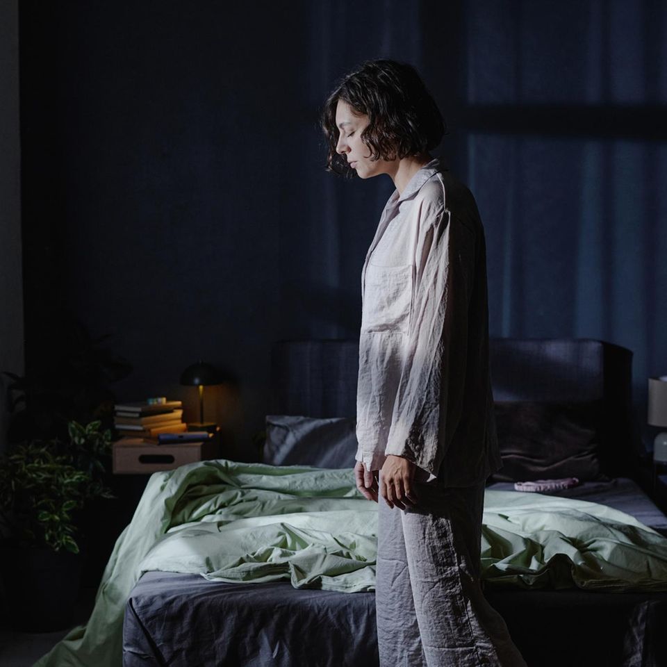 Frau mit Schlafstörungen steht im Schlafanzug müde vor ihrem Bett