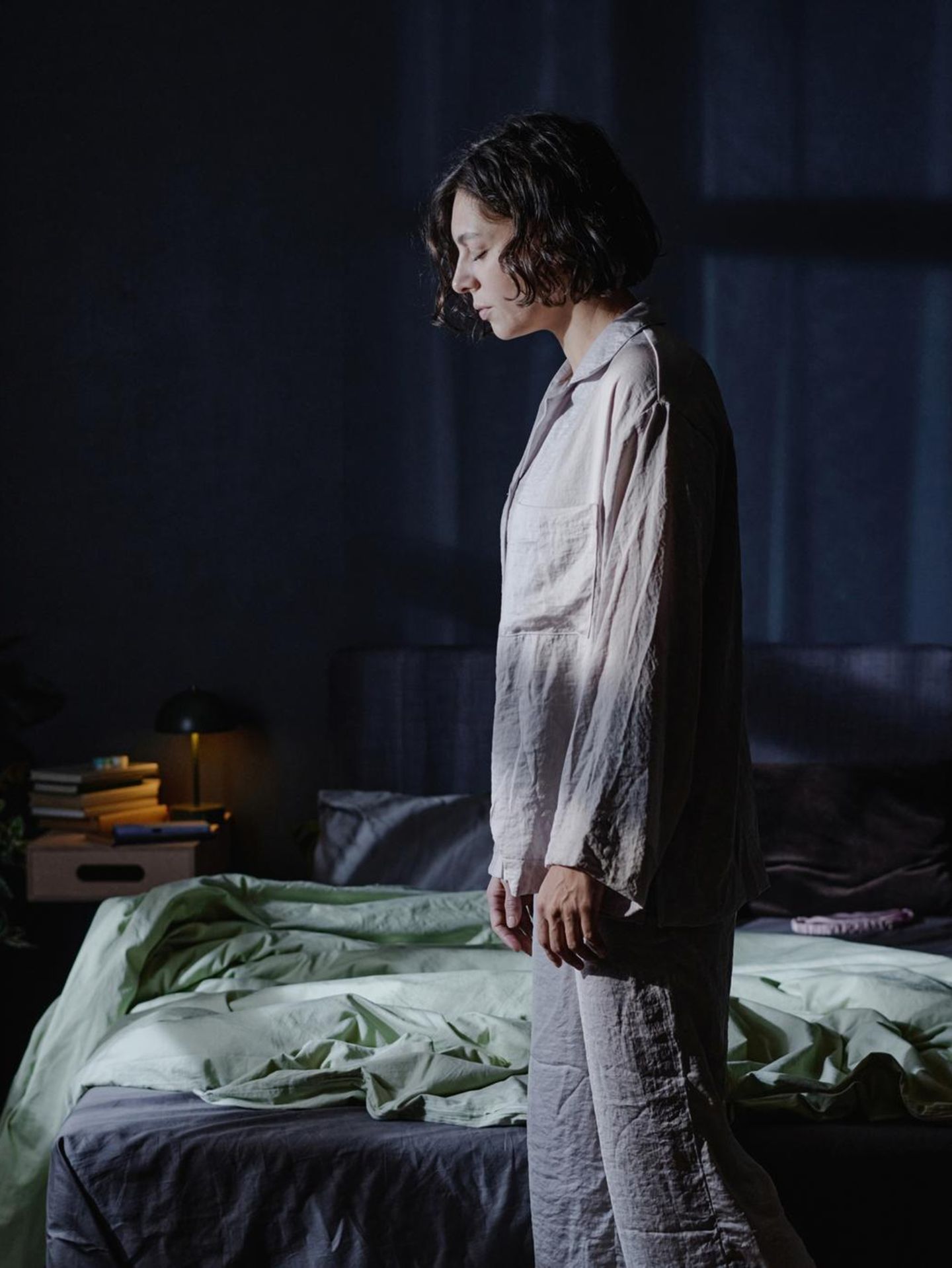 Frau mit Schlafstörungen steht im Schlafanzug müde vor ihrem Bett