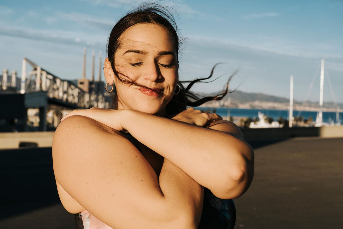 Eine Person umarmt sich selbst und steht mit geschlossenen Augen im Sonnenlicht