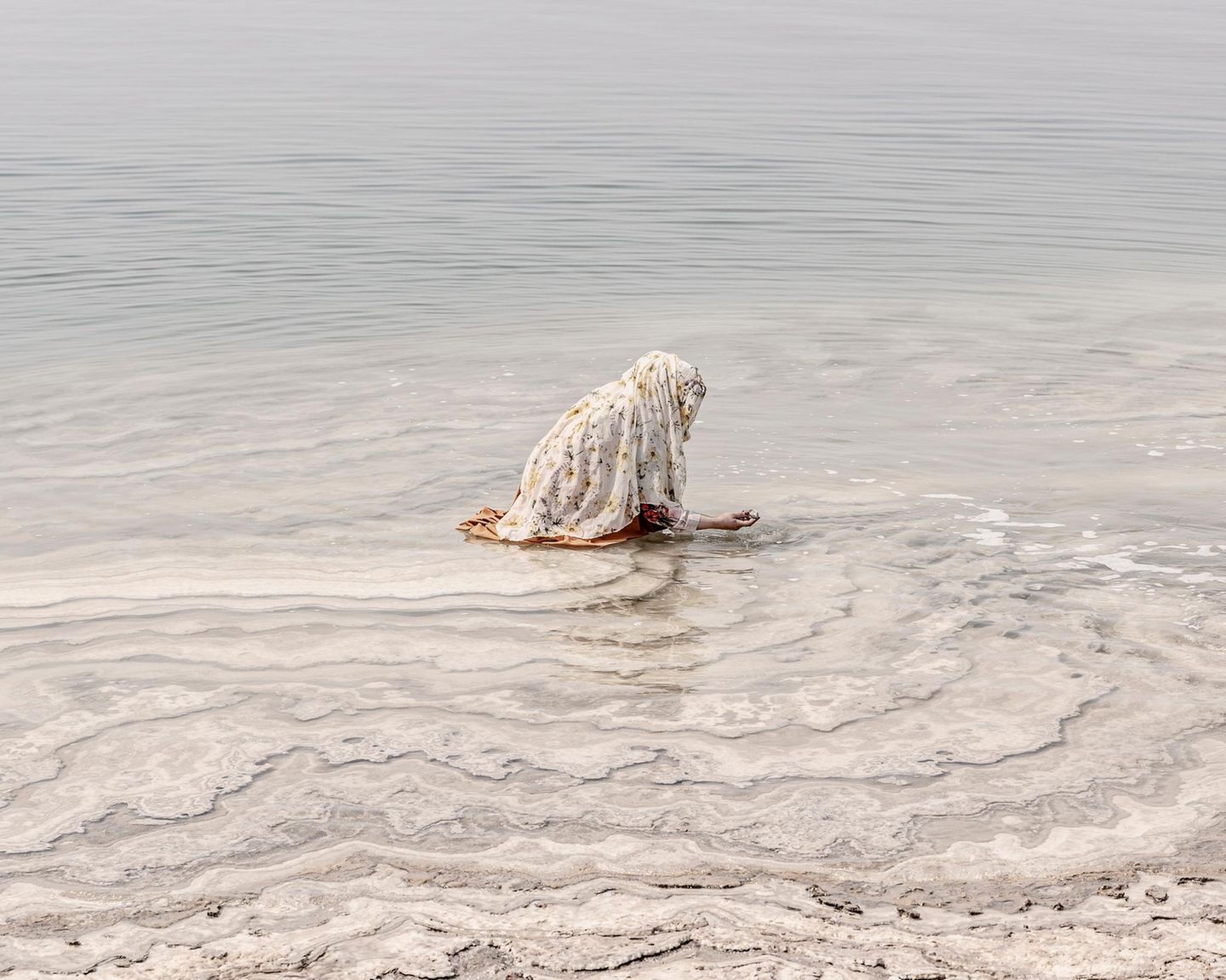 Am Ufer des Toten Meeres, in Jordanien, hockt eine Frau im flachen Wasser und tastet nach Salzsteinen. Beinahe entrückt erscheint die Szene und sie ist Teil einer Jahrtausende alten Tradition: Den Mineralen des hypersalinen Sees wird eine reinigende und heilende Wirkung zugeschrieben. Das Salz soll die Haut beruhigen, die Muskeln entspannen, kleine Wunden versiegeln. In Jordanien gehören Rituale der Pflege und Reinigung für viele zum Alltag, wobei sie heute auch in die Wellnessindustrie und den Tourismus reichen.   Die Aufnahme ist Teil des internationalen "Walk of Water"–Fotowettbewerbs von UNESCO und Onewater. Die ausgezeichneten Bildgeschichten zeigen, wie eng Wasser mit Identität und Kultur verwoben ist – von rituellen Gesten bis zum alltäglichen Überleben.