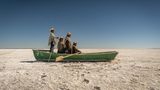 Auf der schier endlosen Salzfläche des ausgetrockneten Poopó-Sees versammeln sich Florencio, Pablo, Cipriana und Félix Mauricio in einem Boot. Ein Relikt aus Zeiten, in denen hier noch Fische statt Staub ihr Dasein bestimmten. Die Qotzuñi haben ihre traditionelle Existenz verloren: Mit dem Klimawandel, dem Wasserentzug für Landwirtschaft und Bergbau verschwand eines der größten Binnengewässer Boliviens fast vollständig. Heute widmet sich die Gemeinschaft dem Kunsthandwerk, um Erinnerung und Identität zu bewahren. Die Inszenierung auf der dürren Ebene ist eine Art Denkmal: für eine Kultur, die sich neu erfinden musste, und für ein Ökosystem, das nicht zurückkehren wird.