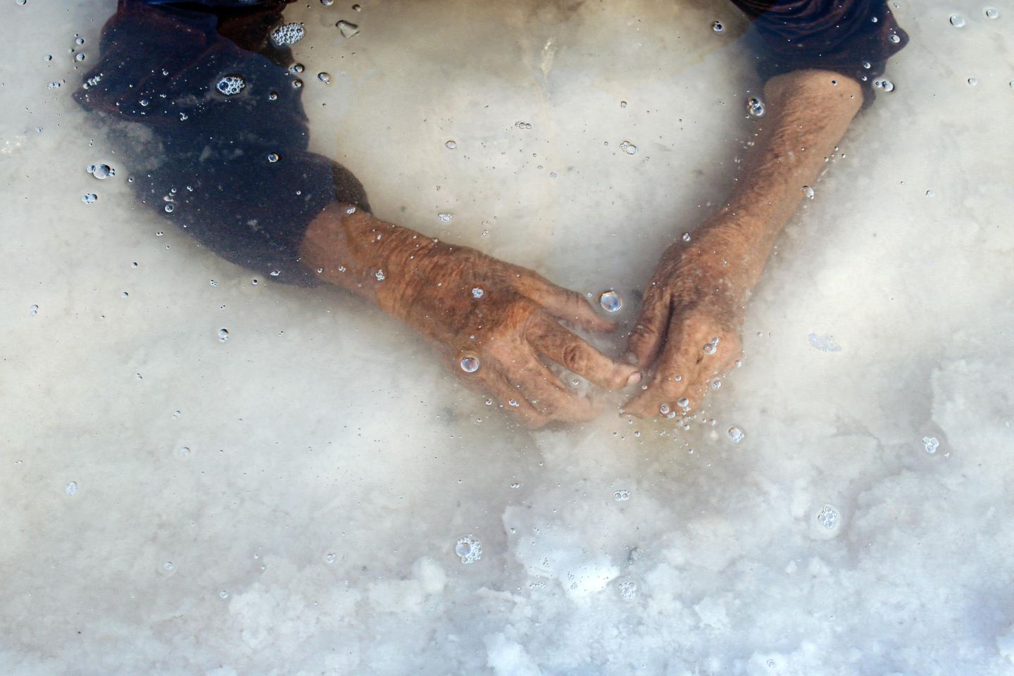 In das seichte Wasser des fast ausgetrockneten Urmia-Sees tauchen die Hände einer älteren Frau, es ist die Großmutter der Fotografin Solmaz Daryani. Die Haut ist vom Leben gezeichnet, der See vom Klimawandel. In das einst größte Binnengewässer des Irans hätte noch in den 1990er Jahren der Bodensee neunmal hineingepasst. Heute bleibt vielerorts nur eine kristalline Kruste und flaches Restwasser zurück. Die Geste der Großmutter ist unscheinbar und zugleich tief: ein Prüfen, Tasten, vielleicht ein Erinnern an Zeiten, in denen der See noch ein Ort des Badens, der Erholung und des Alltags war. Und so verbindet das Bild eine persönliche Geschichte mit einer ökologischen Tragödie.