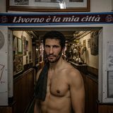 Im historischen Stadtteil Borgo Cappuccini im italienischen Livorno steht Karim Rachedi vor dem Eingang eines lokalen Clubs. Der Blick des Athleten wirkt ruhig. Und  dabei auch ein Stückweit herausfordernd. "Livorno ist meine Stadt" prangt auf dem Schal hinter dem Ruderer; ein kurzer Satz, der sportliche Disziplin mit Zugehörigkeit verknüpft. Denn das Rudern fordert hier nicht bloß Wettkampfsgeist. Es prägt auch Identität: ein kollektives Ritual zwischen Hafen und Meer, Wohnhäusern und Vereinsraum. Die Pokale im Hintergrund erzählen von Siegen, Jubel, Tradition. 