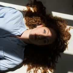 Eine Frau liegt entspannt auf dem Rücken. Sonne fällt durch ein Fenster auf ihr Gesicht