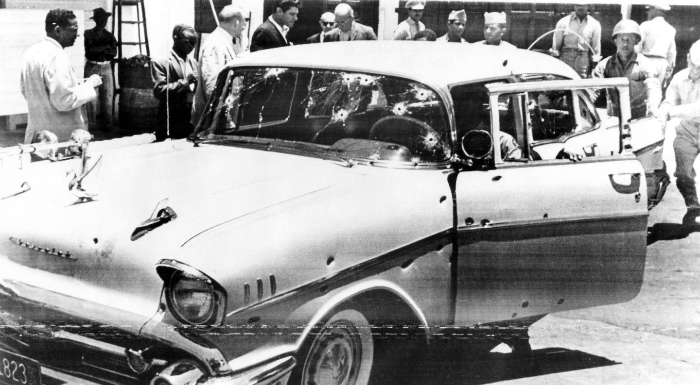 Ein Auto ist an Karosserie und Scheiben durchlöchert von Schüssen