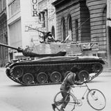 Ein Panzer steht auf einer Straßenkreuzung, beobachtet von einem Mann mit Fahrrad