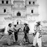 Fünf Männer mit Hüten und Gewehren stehen vor einer Kirchenfassade
