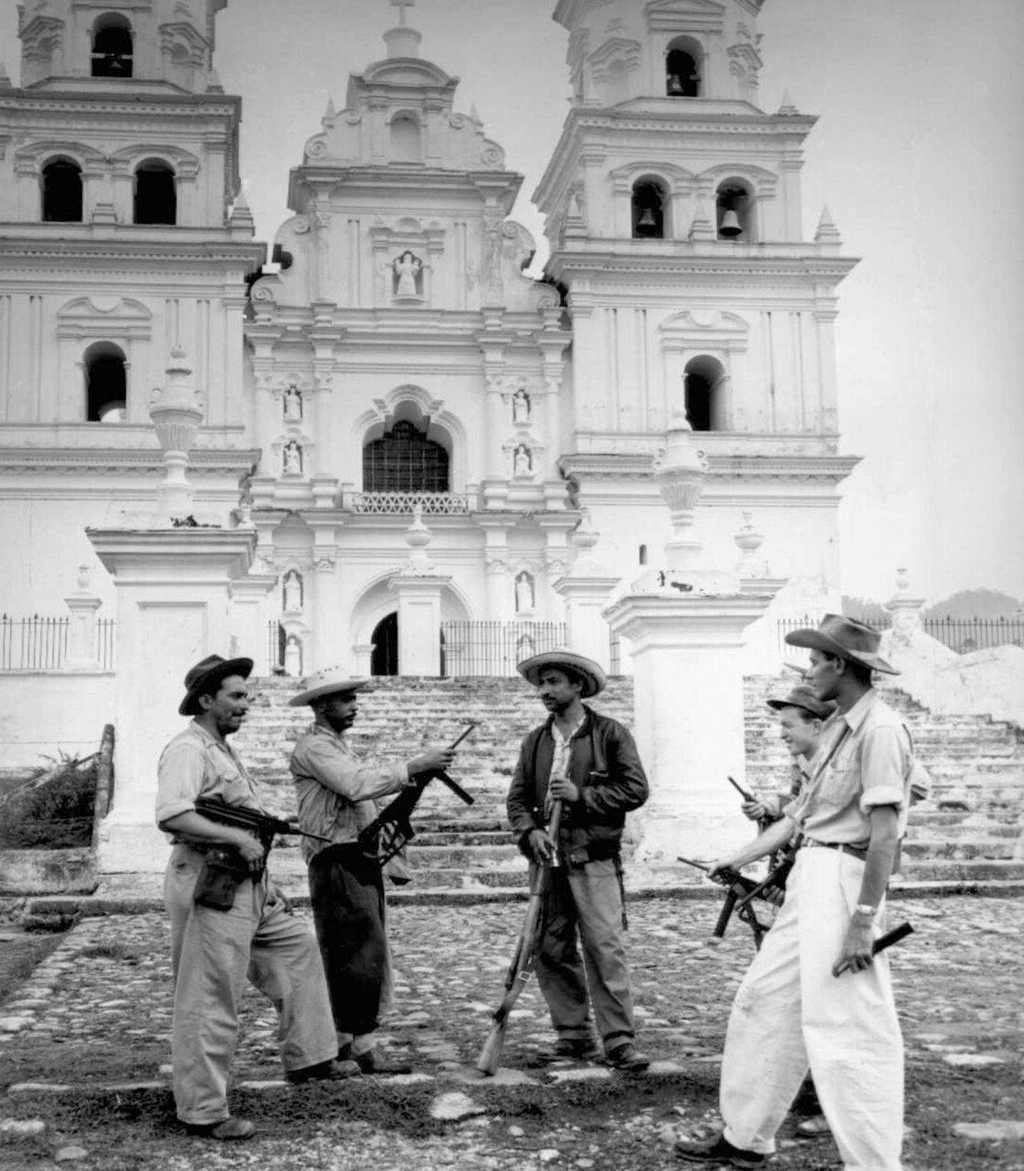 Fünf Männer mit Hüten und Gewehren stehen vor einer Kirchenfassade