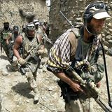 Stark bewaffnete US-Kämpfer laufen durch eine steinige, enge Gasse