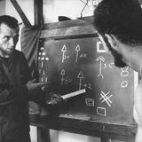 Ein Mann instruiert einen zweiten an einer Tafel voller Zeichen