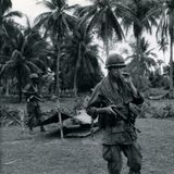 Ein US-amerikanischer Soldat steht rauchend vor Palmen