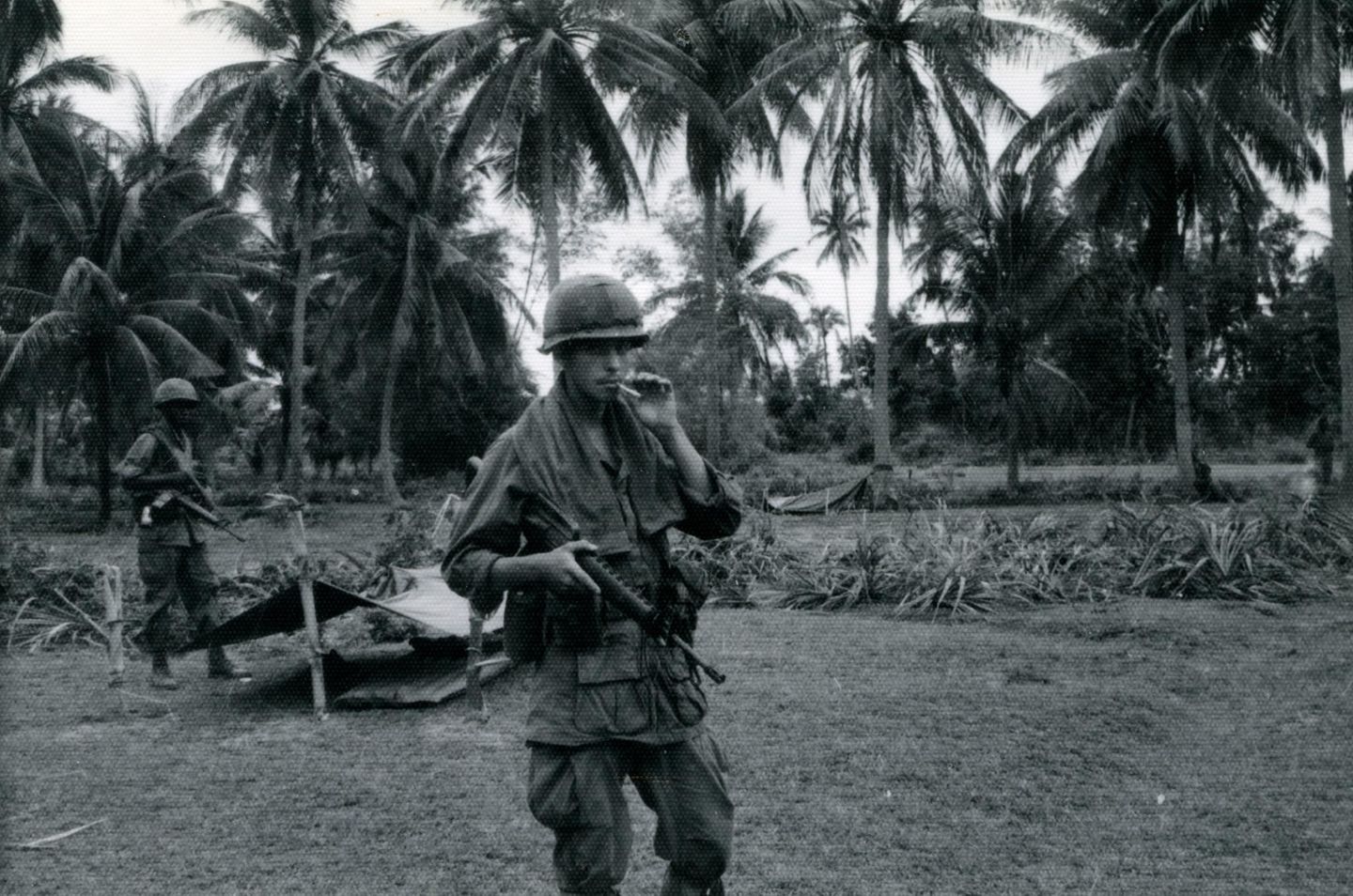 Ein US-amerikanischer Soldat steht rauchend vor Palmen