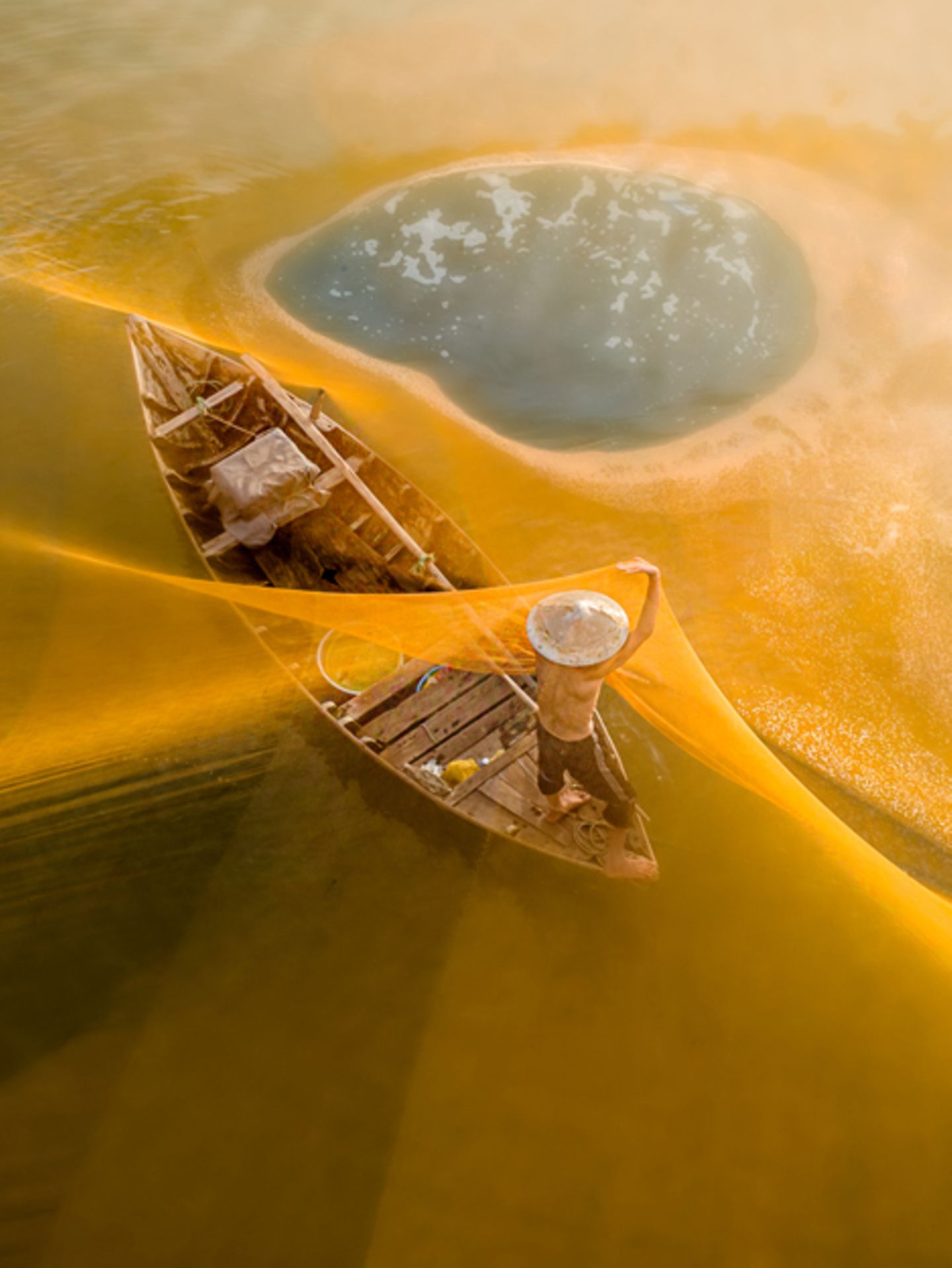 Im Morgenlicht leuchten die Netze golden über einem Fluss in Vietnam. Die Fischer spannen sie für ihren Fang weit übers Wasser. Auf Teo Chin Leongs Foto ist der Fang nicht zu sehen. Die sanften Farben und die klare Komposition lassen die Szene friedlich wirken, fast wie in einem Traum oder einer Fantasie.