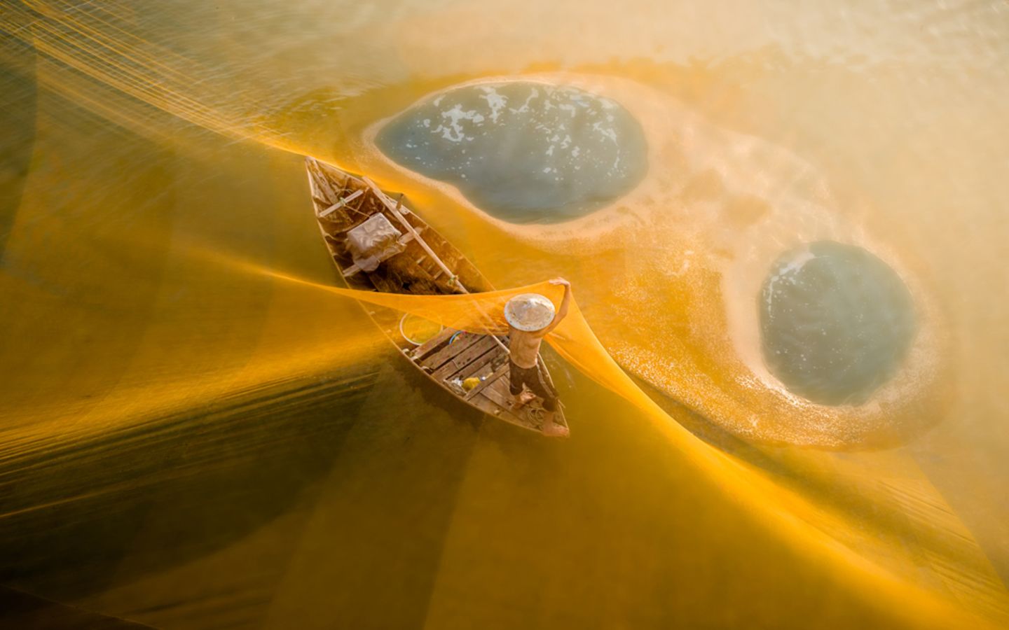 Im Morgenlicht leuchten die Netze golden über einem Fluss in Vietnam. Die Fischer spannen sie für ihren Fang weit übers Wasser. Auf Teo Chin Leongs Foto ist der Fang nicht zu sehen. Die sanften Farben und die klare Komposition lassen die Szene friedlich wirken, fast wie in einem Traum oder einer Fantasie.