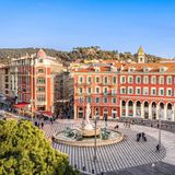 Trotz seiner Größe wirkt der Platz fast gemütlich: Pflastersteine im Schachbrett-Design, rostrote Fassaden und elegante Arkaden prägen den Place Masséna, das pulsierende Herz Nizzas. Ab und zu zieht die Straßenbahn vorbei und vervollständigt das geschäftige Treiben. Über allem wacht die sieben Meter hohe Statue des Apollo auf dem Fontaine du Soleil, dem "Sonnenbrunnen". Einst sorgte die vermeintlich übermäßige Nacktheit des Lichtgotts für so viel Empörung, dass seine Statue an den Rand der Stadt verbannt wurde. Erst seit 2011 thront Apollo wieder auf seinem Brunnen – ein toller Startpunkt für einen Stadtbummel. Denn von hier aus sind es nur wenige Schritte zur Promenade des Anglais, in die gemütliche Altstadt oder zur Einkaufsstraße Avenue Jean Médecin. Und wo das Herz der Stadt ist, darf die grüne Lunge nicht fehlen: Direkt nebenan liegt die weitläufige Parkanlage Promenade du Paillon, die zum Spazieren und Verweilen einlädt.