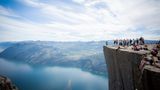 Felsplateau Preikestolen mit Menschen, im Hintergrund Lysefjord, Berge und Himmel