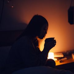 Frau mit Tee am Bett sitzend