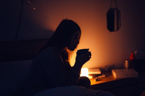 Frau mit Tee am Bett sitzend