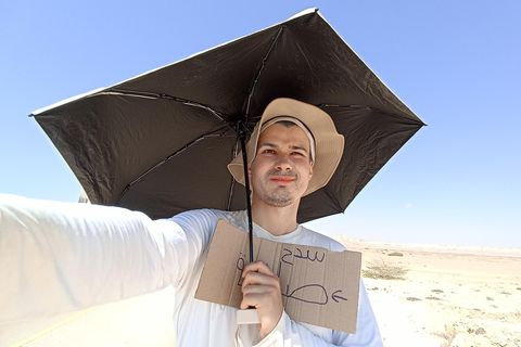 Lukas Stock beim Warten auf ein Auto mit Sonnensegel, Hut und Schild