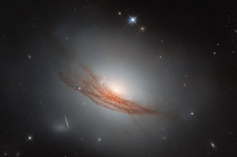 NGC 7722 ist ein kosmisches Zwischenwesen, das Eigenschaften von Spiralgalaxien und elliptischen Galaxien vereint – und doch keiner dieser Gruppen angehört. Forscher zählen sie zu der kleinen, schwer definierbaren Gruppe der linsenförmigen Galaxien. Rund 187 Millionen Lichtjahre von der Erde entfernt erstrahlt die kosmische Schönheit im luftleeren Raum. Sie besitzt den leuchtenden Halo einer elliptischen Galaxie und eine Scheibe, um die konzentrische Staubringe wirbeln. Ihr charakteristischstes Merkmal ist der rostrote Schleier: Schwaden aus Staub winden sich um die leuchtende Mitte der Sterneninsel. Viele linsenförmige Galaxien tragen solch ein diffuses Band. Forschende sehen darin Spuren der Verschmelzung mit einer anderen Galaxie.   2020 verfolgten Astronomen und Astrophysikerinnen gebannt, wie ein Stern in den Sphären von NGC 7722 explodierte. Vorübergehend überstrahlte die Supernova ihre kosmische Nachbarschaft; inzwischen ist sie jedoch verglüht. So gelang es dem Hubble-Weltraumteleskop, diese außergewöhnliche Sterneninsel schärfer einzufangen als je zuvor.  KW06