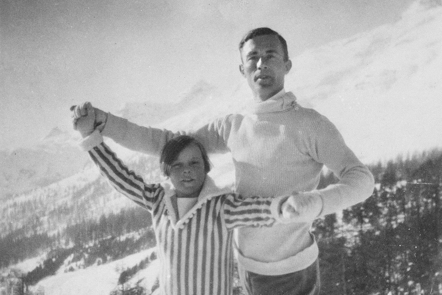 Vor einem Bergpanorama halten sich ein Mann und ein Mädchen  an beiden Händen wie ein Tanzpaar