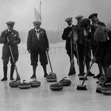 Sieben britische Curlingspieler mit Schiebermützen stehen mit Besen bewaffnet auf dem Eis