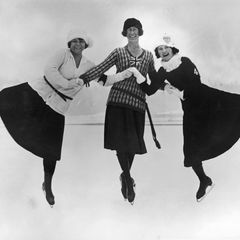 Drei Frauen in Schlittschuhen halten sich über Kreuz an den Händen und springen in die Luft