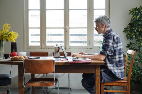 Ein Mann sitzt an seinem Küchentisch und arbeitet am Laptop