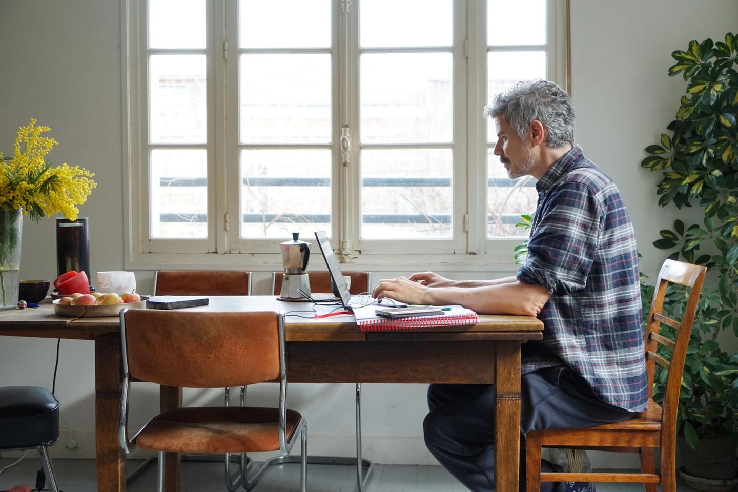 Ein Mann sitzt an seinem Küchentisch und arbeitet am Laptop