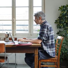Ein Mann sitzt an seinem Küchentisch und arbeitet am Laptop