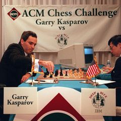 An einem Schachbrett sitzen sich Kasparow und ein Mann mit einem PC gegenüber.