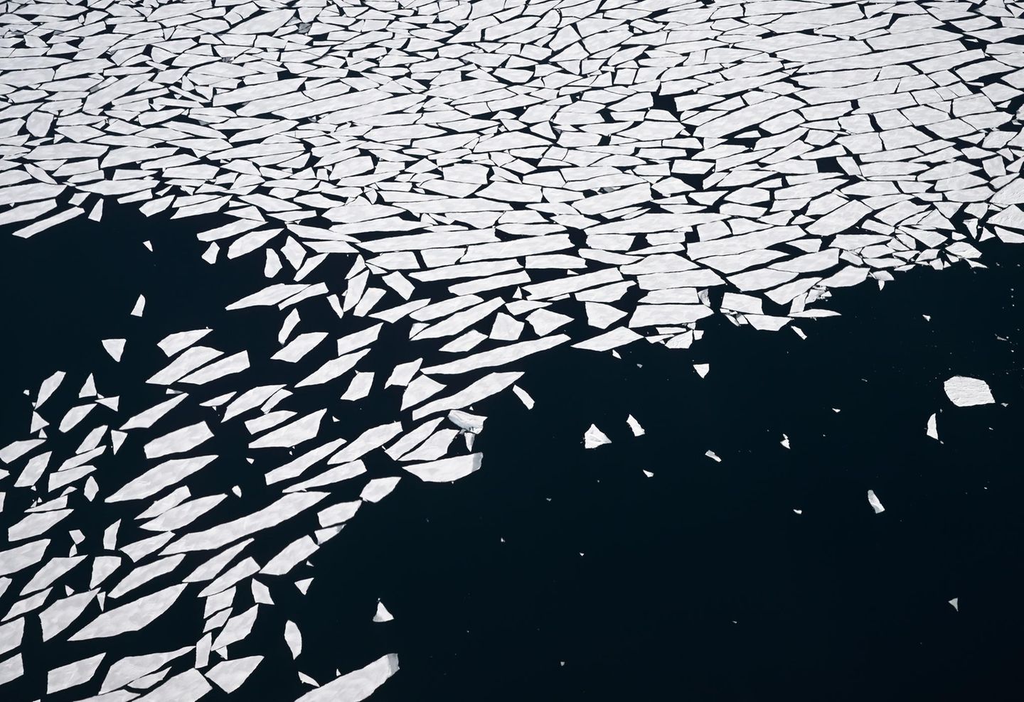 Wie Splitter einer geborstenen Milchglas-Scheibe muten diese in der Diskobucht treibenden Eisschollen an. Dass das umgebende Wasser schwarz erscheint, ist der Vogelperspektive geschuldet: Von oben gesehen, sind Spiegelungen des Himmels auf ein Minimum reduziert.