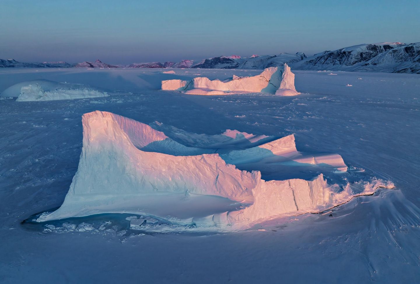 Im Schein der untergehenden Sonne leuchten die Spitzen der im Uummannaq-Fjord eingefrorenen Eisberge noch einmal in zarten Rosa-Tönen auf. "Das Licht, die spirituelle Erhabenheit des Panoramas und wohl auch die schiere Kälte raubten mir vor Ort oft den Atem", schreibt der Fotograf. "Mit der Drohne konnte ich das Spiel der letzten Sonnenstrahlen auf den Eisbergen aus der Vogelperspektive einfangen, während mir die Weite des Eises als bequeme Start- und Landefläche zur Verfügung stand".