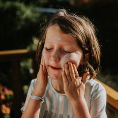 Ein Kind cremt ihr Gesicht mit Sonnencreme ein